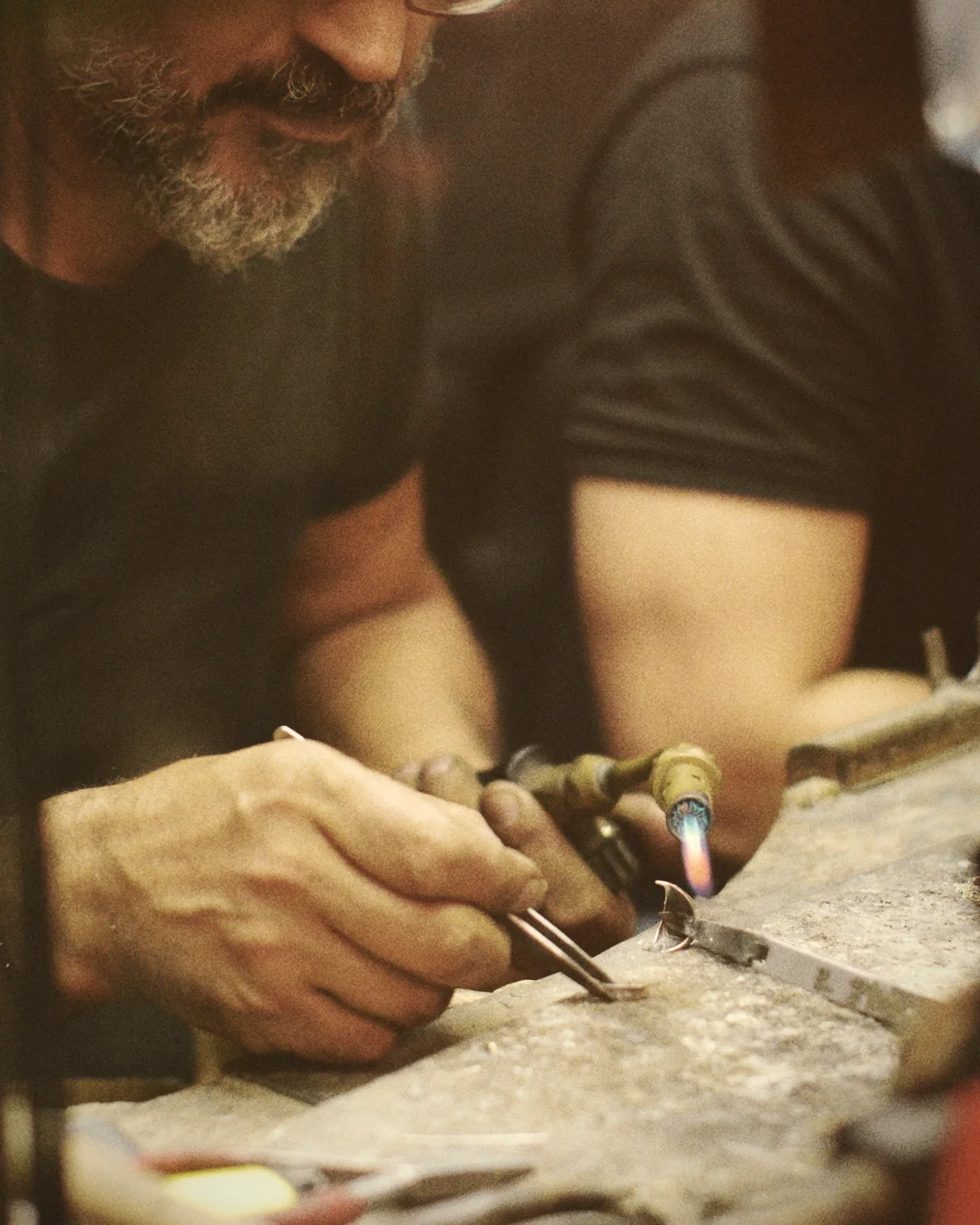 A craftsman soldering metal with a torch at his workbench