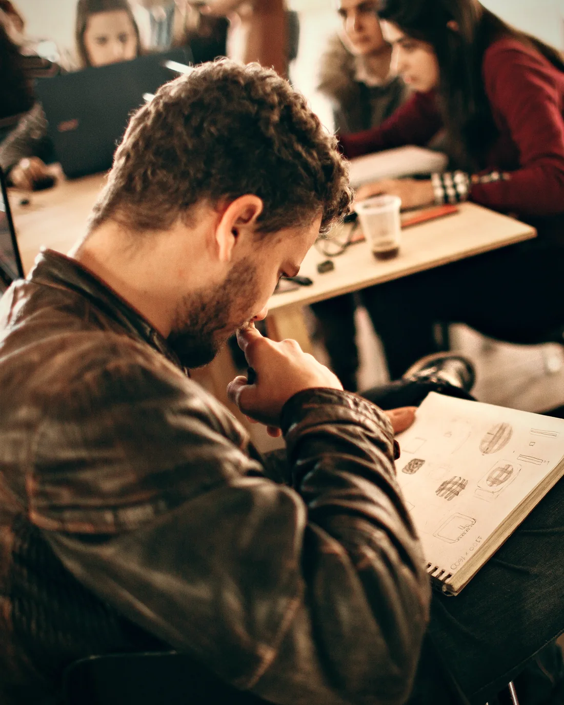 Someone studying a notebook of sketches at a shared work table