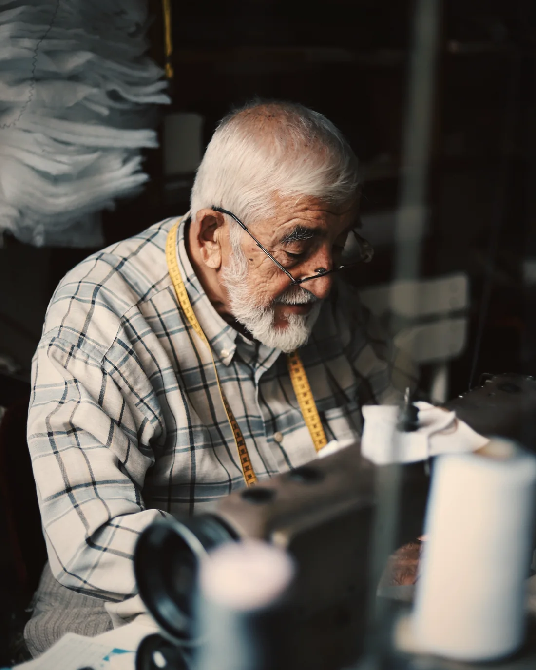 An elderly tailor at his sewing machine, focused on his craft
